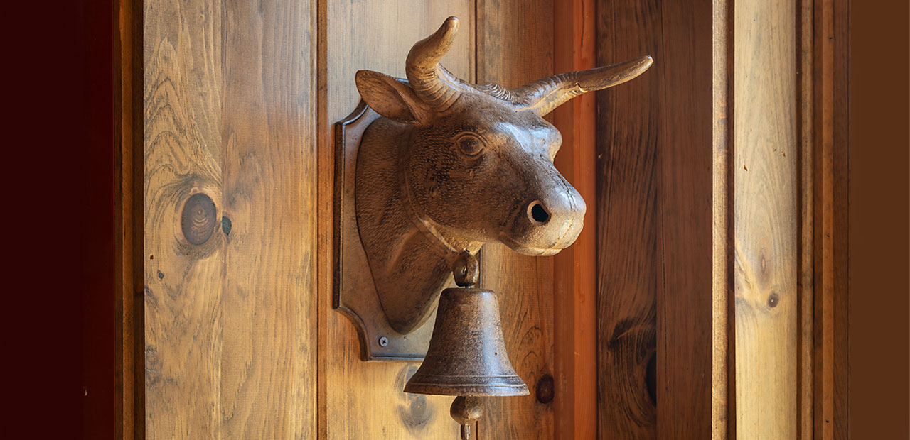 An antique metal cow ornament and bell hanging on the wall